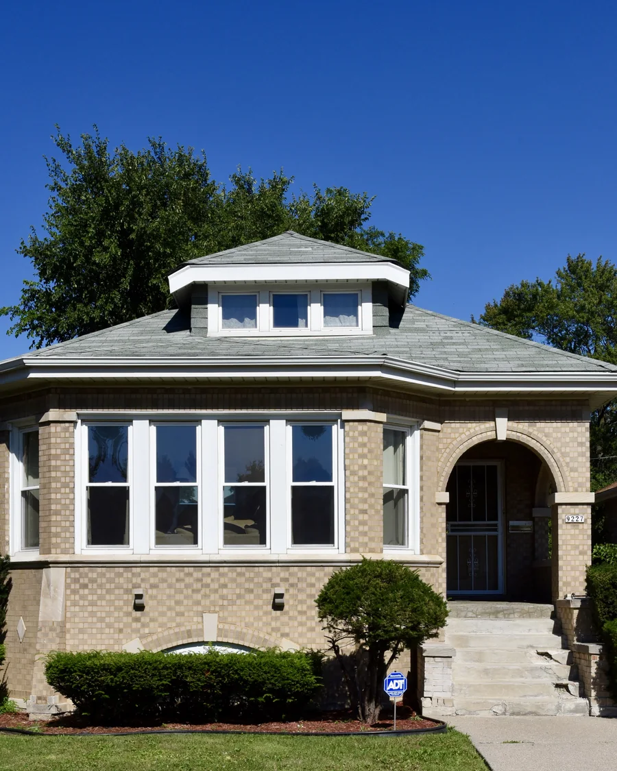 A classic buff-brick Chicago bungalow with a hipped roof and arched entry in a Chicago historic district